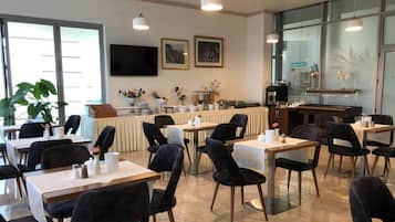 A dining area with tables and chairs, a counter with a cash register, and framed artwork on the wall.