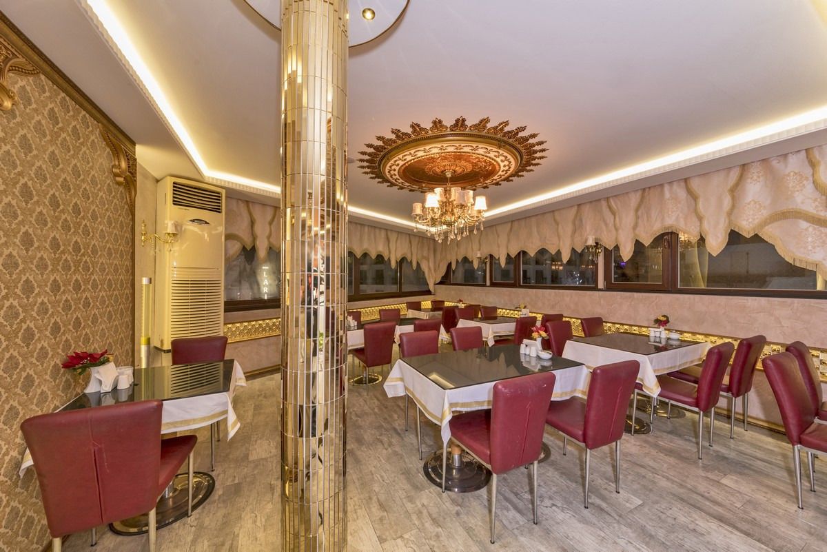 A formal dining area with round tables, red upholstered chairs, and a large chandelier.