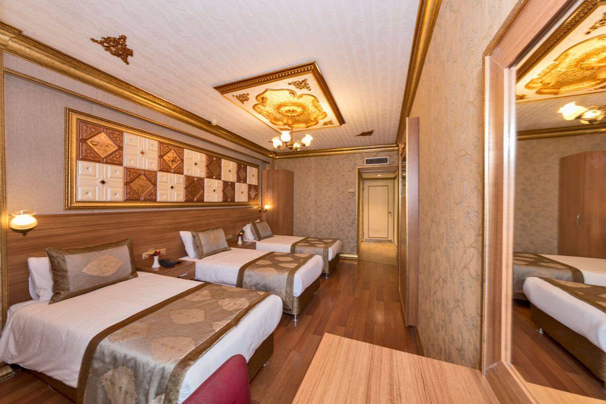 A hotel room with three beds, a large mirror, and a decorative ceiling.