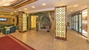 A lobby with a reception desk, a television, a fire extinguisher, and a decorative wall with a faux rock formation. - Version Hotel (Istanbul)