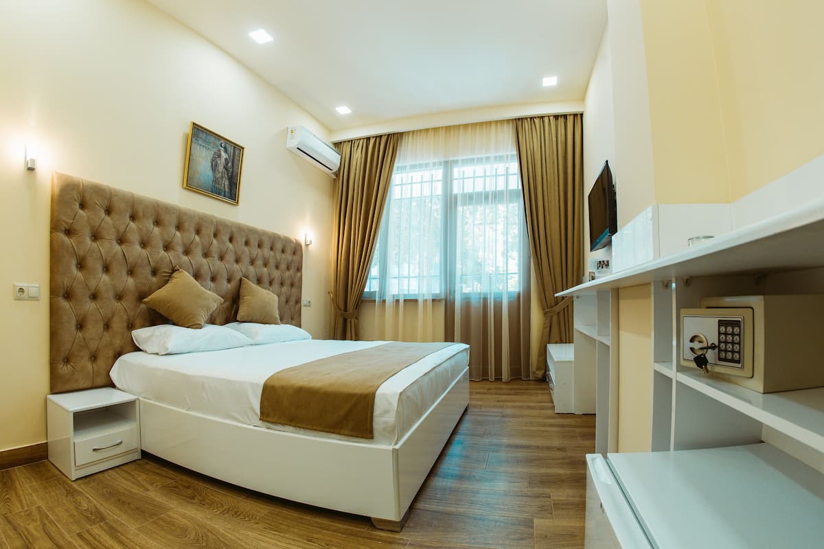 Ein Hotelzimmer mit einem bettigen Bett mit Quasten, einem Nachttisch, einem Fernseher und einer Minibar.