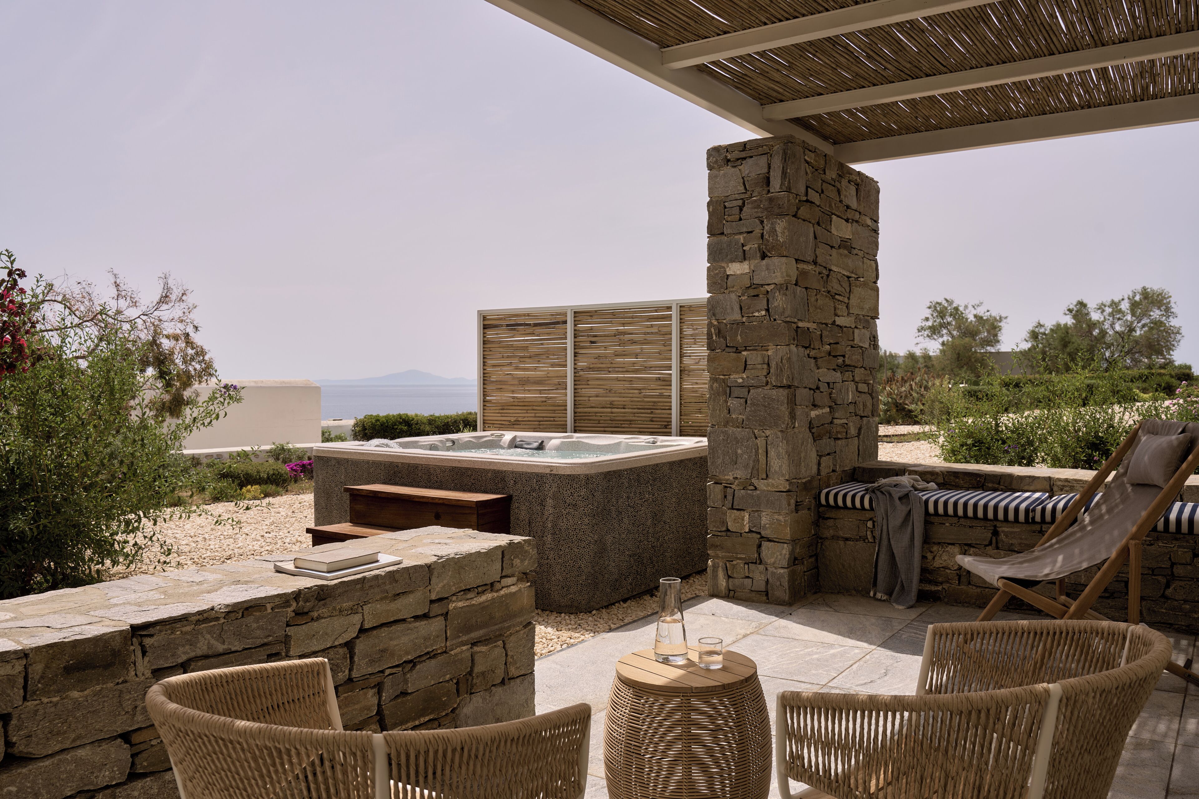 Un jacuzzi con paredes de piedra, mobiliario de mimbre y vistas del paisaje.