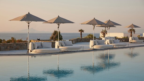 A poolside area with lounge chairs and umbrellas, a stone wall, and a view of the sea.