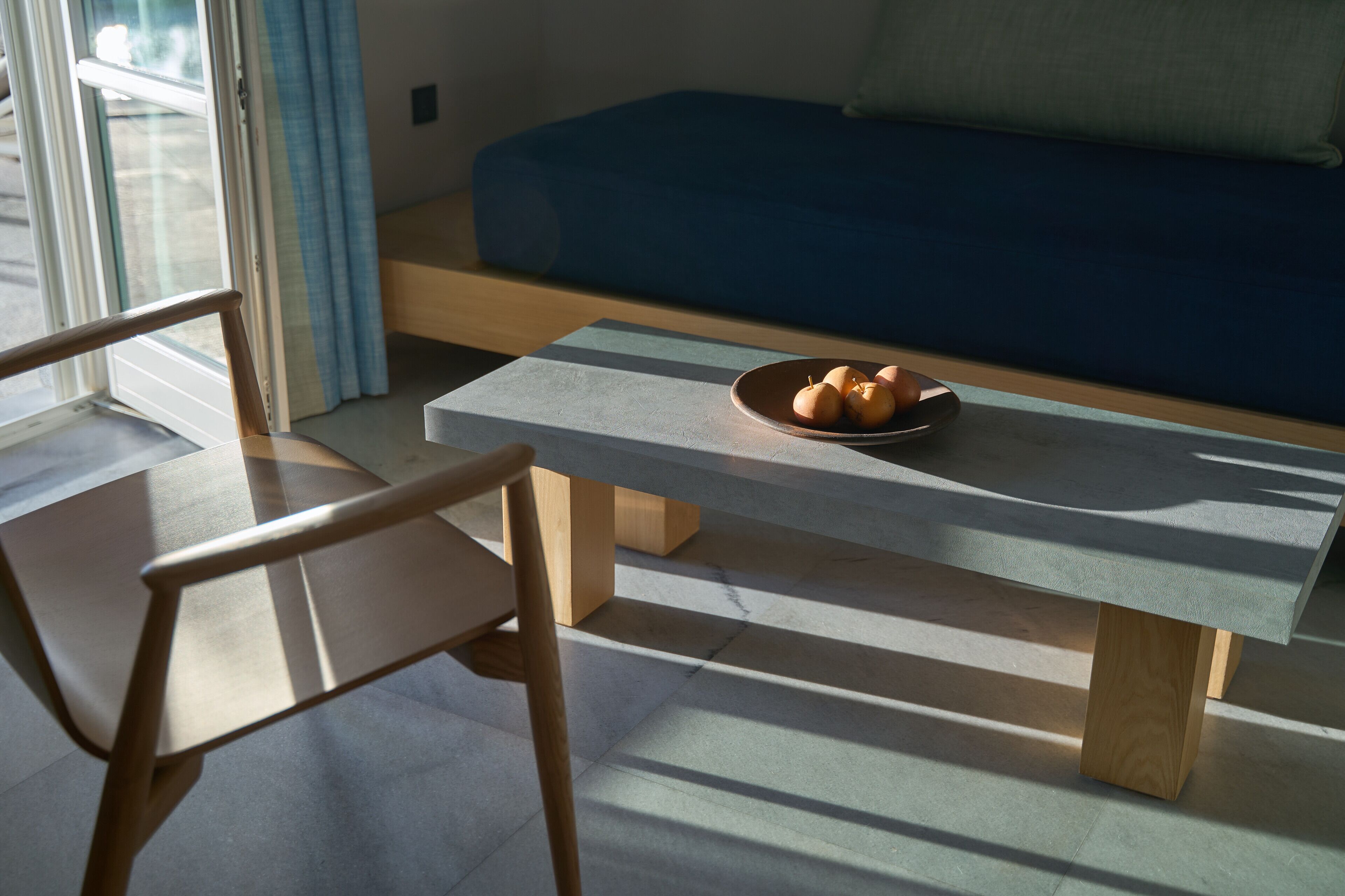A modern room with a blue sofa, a wooden chair, and a table with a bowl of fruit.