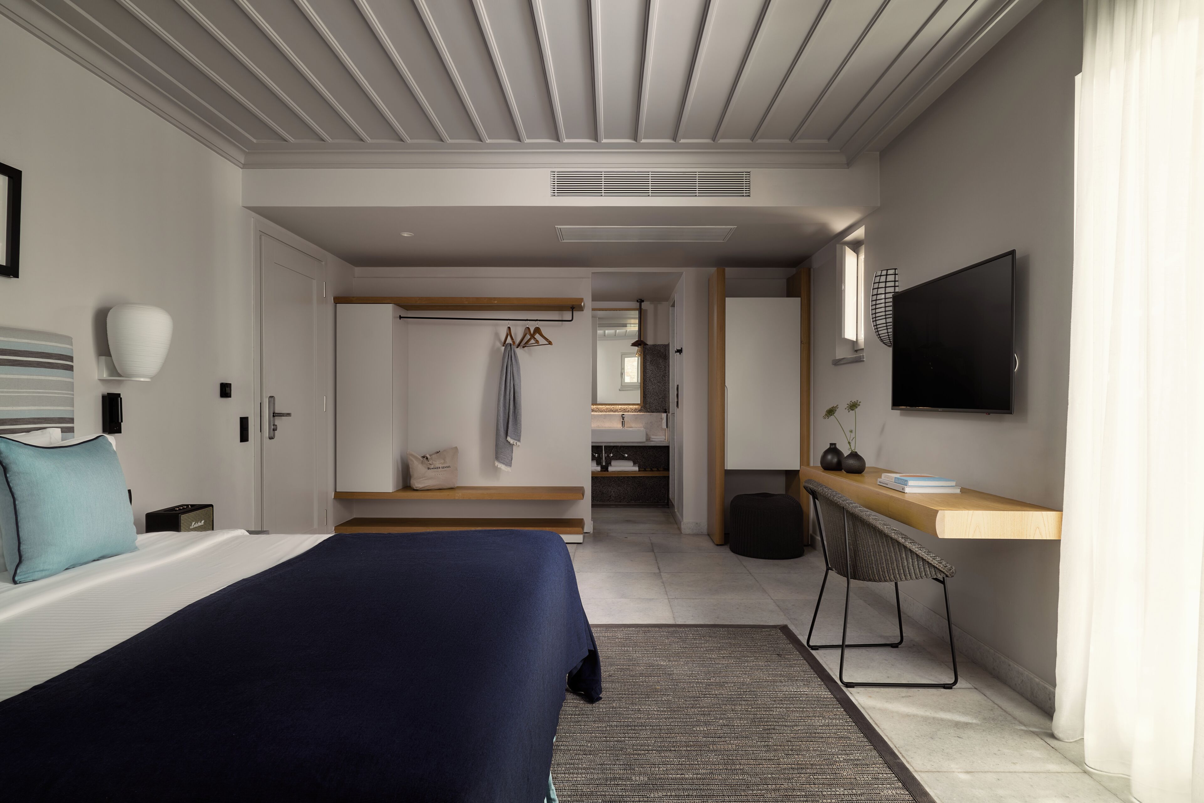 A modern hotel room with a bed, a desk, a TV, and a bathroom visible through an open door.