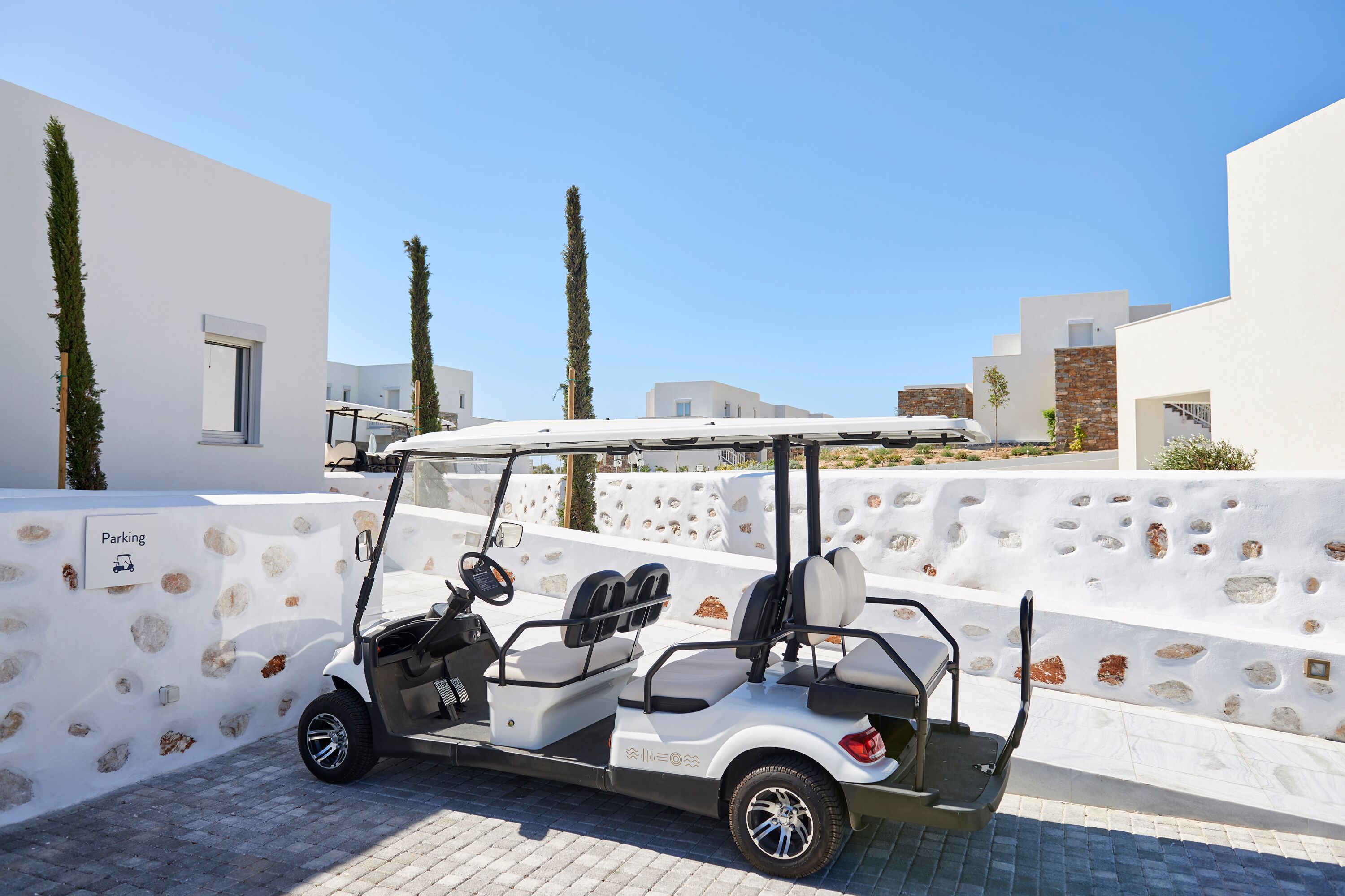 Un carrito de golf blanco estacionado frente a un edificio con un muro de piedra y un letrero que indica una zona de estacionamiento.