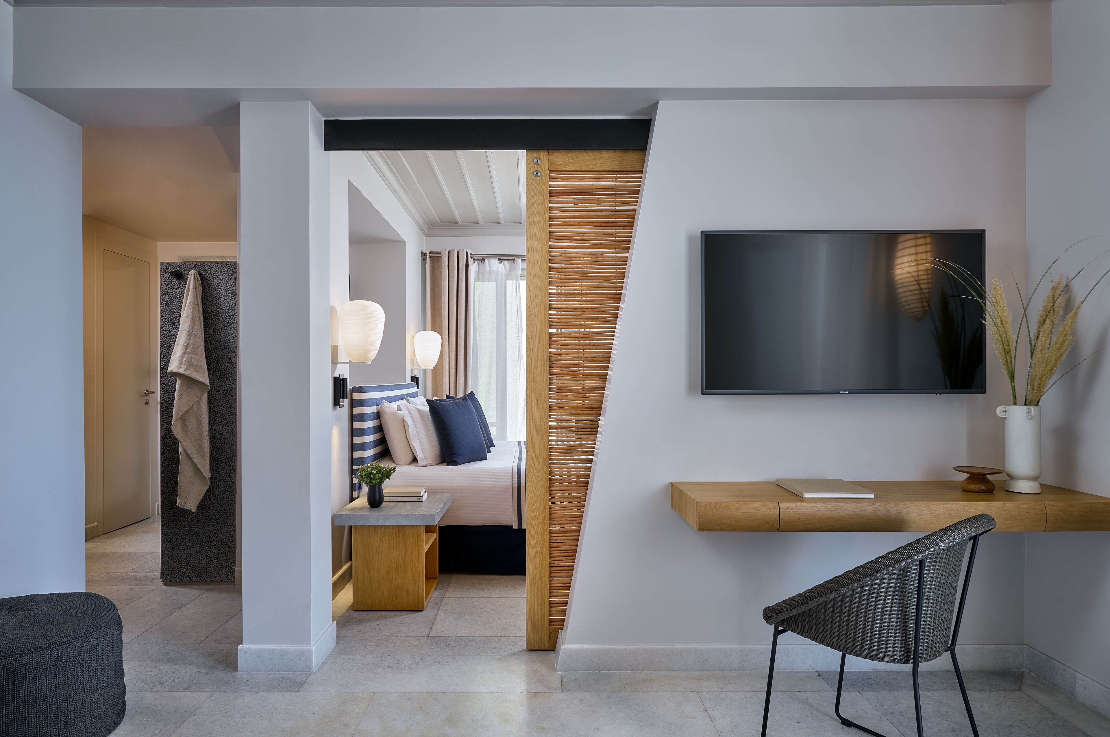 A modern hotel room with a bed, a desk, a TV, and a seating area.
