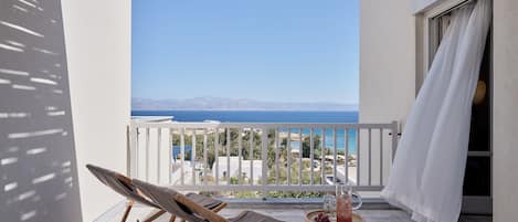Een balkon met uitzicht op zee, een rieten mand en een loungestoel.