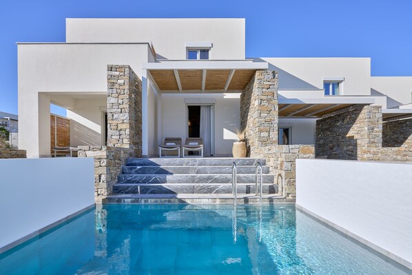 A modern poolside area with a clear blue pool, stone walls, and a covered seating area with two chairs. - Summer Senses Luxury Resort (Paros)