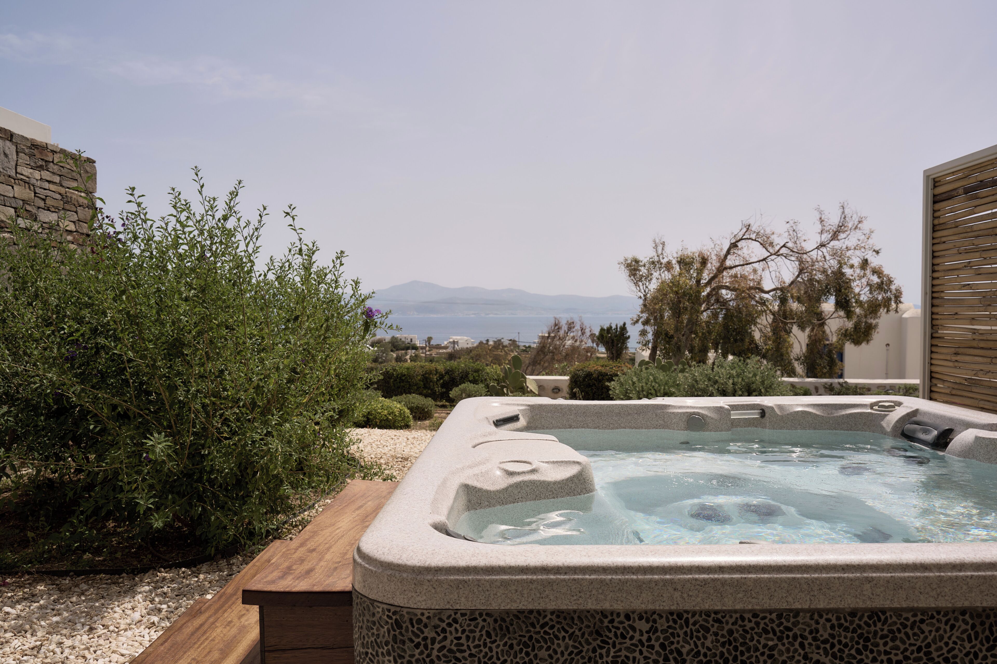 Un jacuzzi con vistas a montañas, rodeado de follaje y una terraza de madera.
