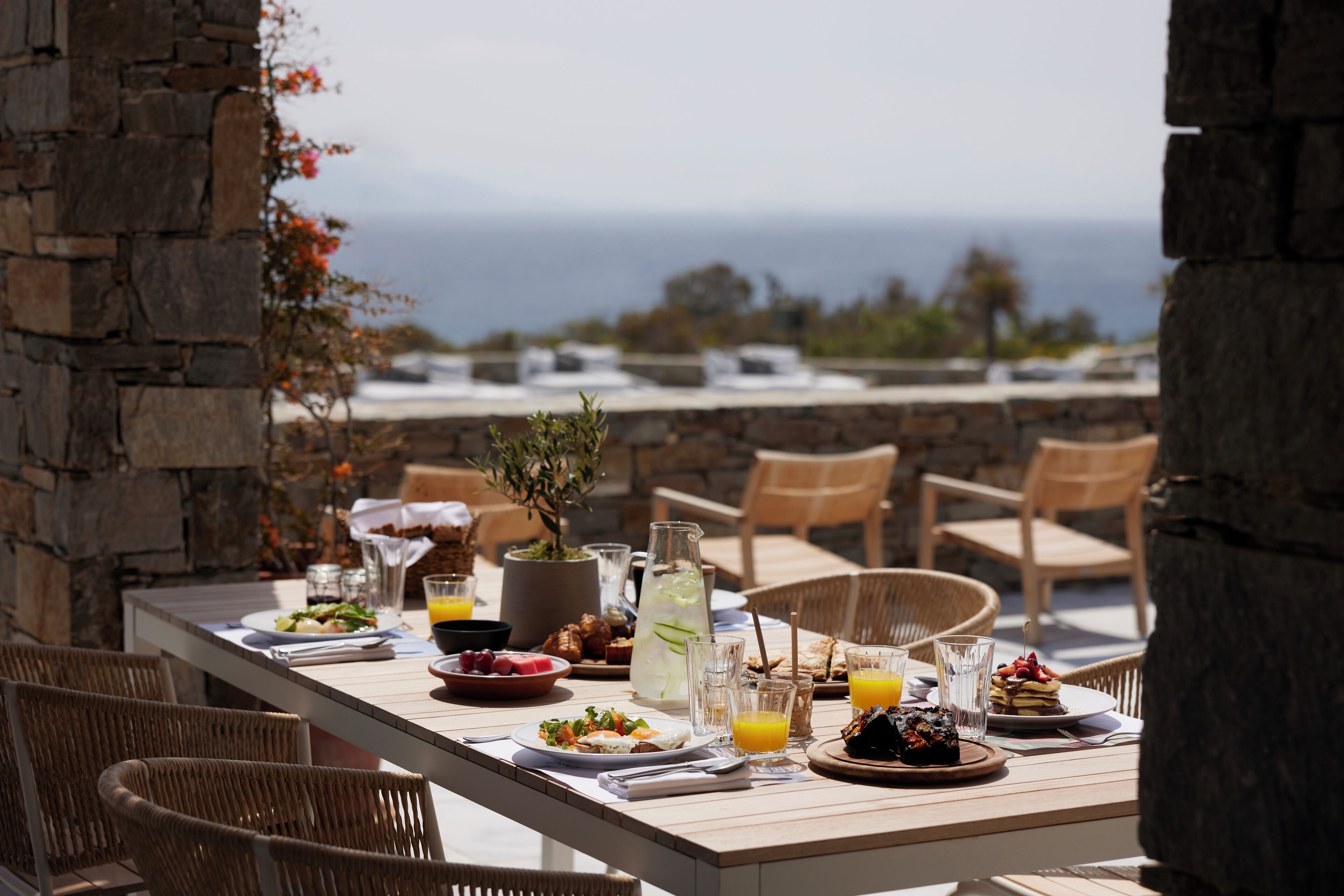Une table de petit-déjeuner dressée avec différents plats et boissons, offrant une vue panoramique sur la mer.