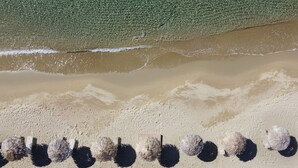 An aerial view of a beach with a row of seaweed balls and a clear view of the ocean waves.