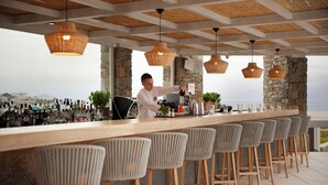 A bar area with a long counter, multiple stools, and hanging wicker lights.