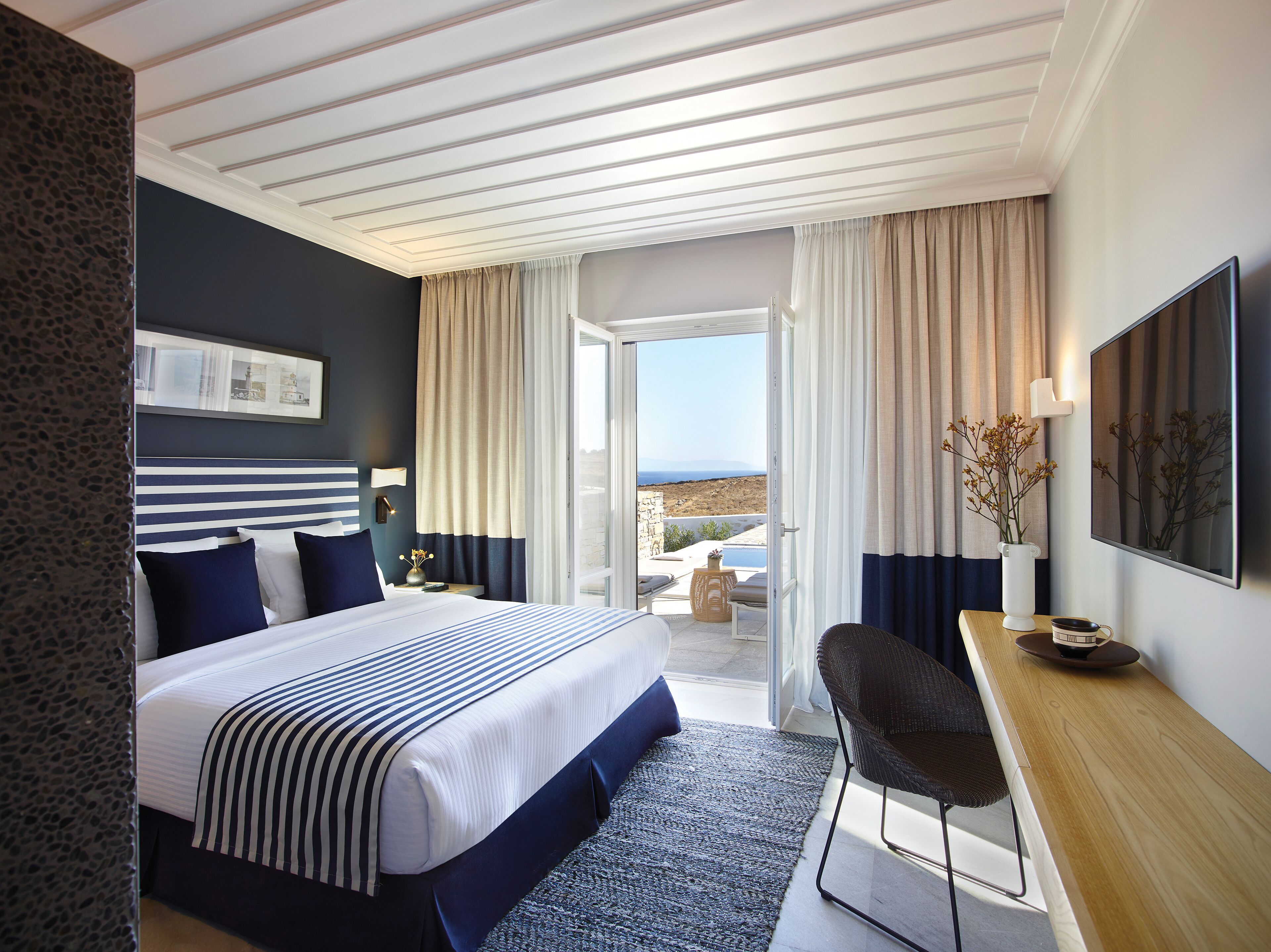 A hotel room with a bed, a desk, and a view of the outdoors.