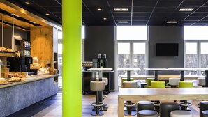Um café moderno com um pilar verde vibrante, balcão de café e áreas de estar com bancos e mesas.