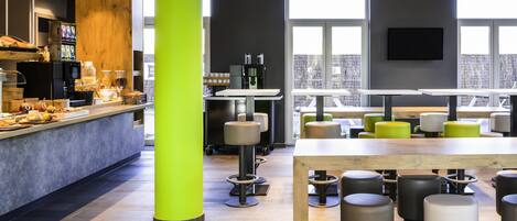 Een modern café met een felgroene zuil, een koffiebar en zithoeken met krukken en tafels.