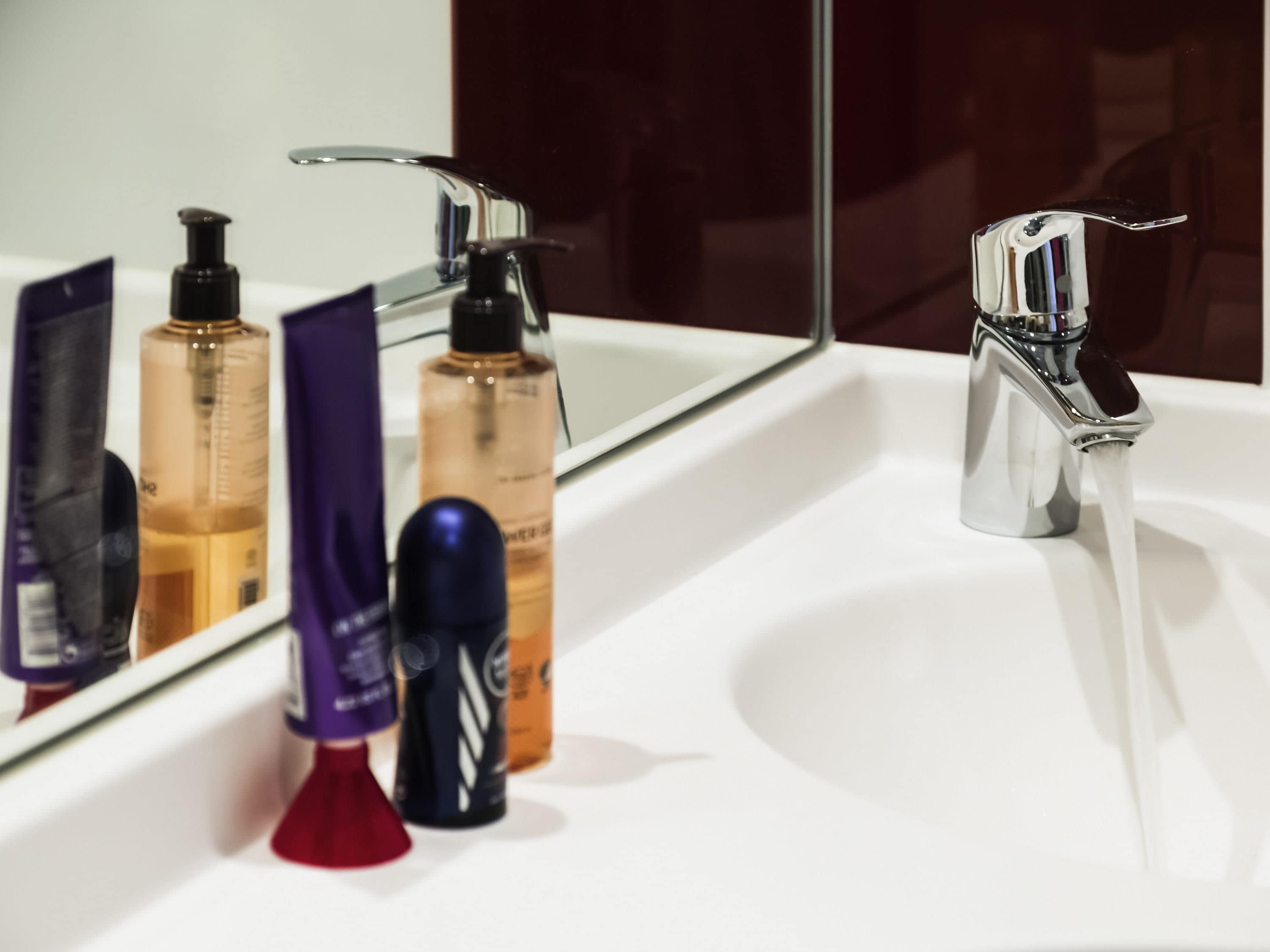 A bathroom sink with a mirror, a faucet, and various toiletries.