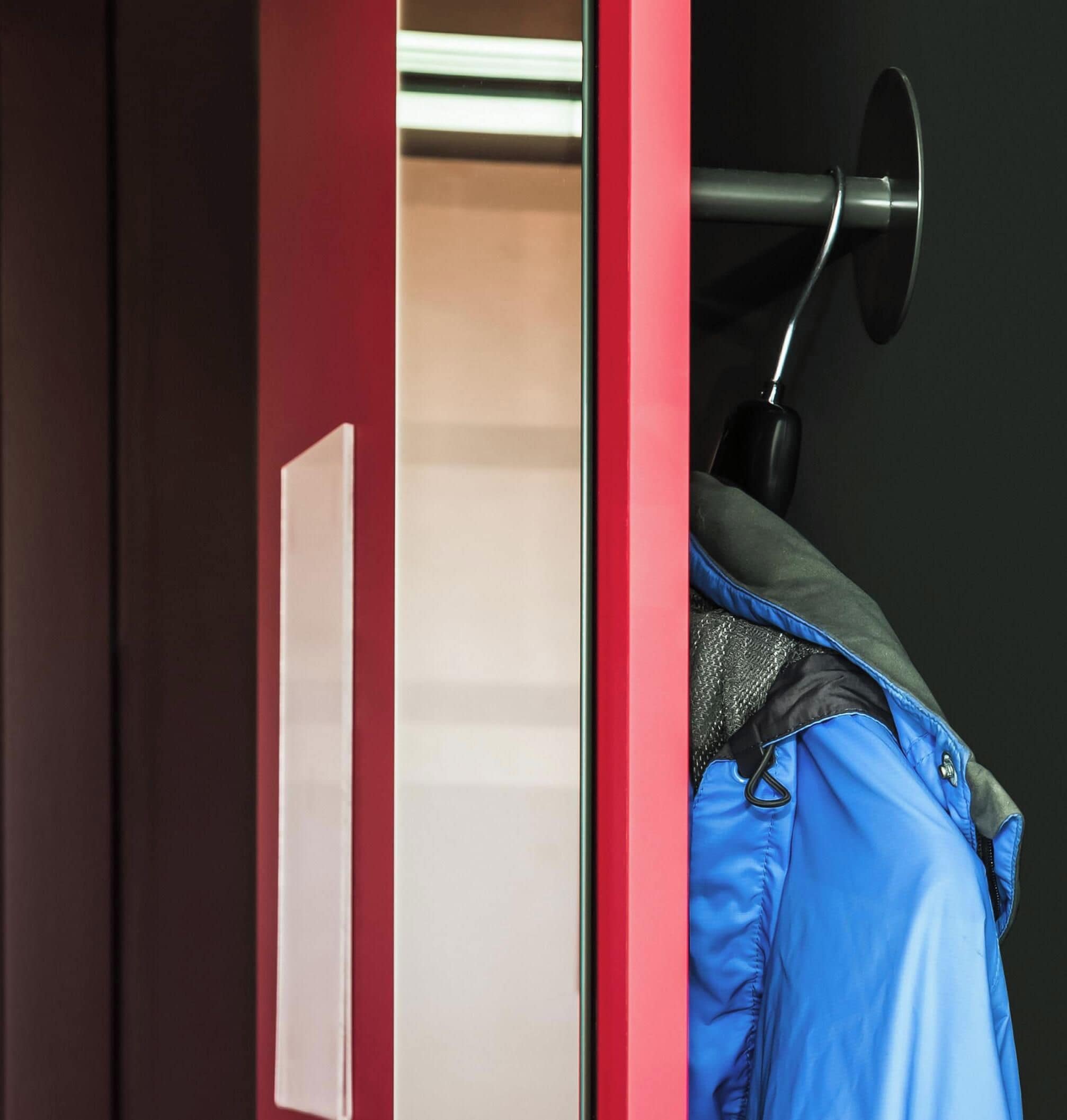 Una puerta roja con un picaporte blanco, una chaqueta azul colgada de un gancho y un objeto negro en la pared.