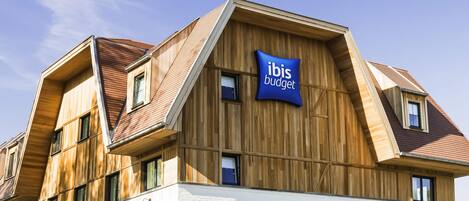 A modern hotel with a wooden facade, multiple windows, and a sign for ibis budget hotel.