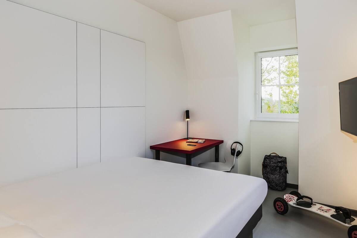 Un dormitorio moderno con una cama, un escritorio, una silla, un televisor y una patineta.