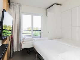Una habitación de hotel con cama, televisión, ventana con cortinas y balcón.