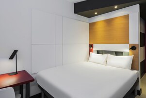 Una habitación de hotel moderna con una cama grande, un escritorio con lámpara y un armario empotrado.