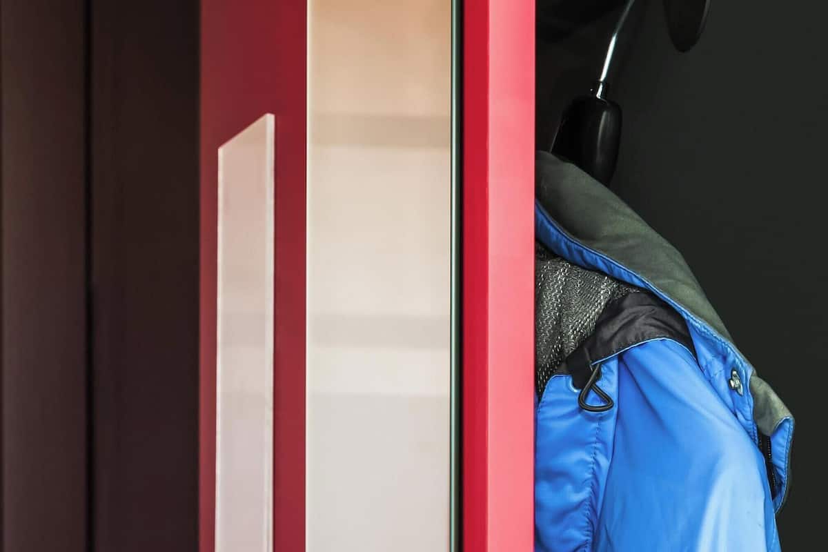 A blue jacket hanging on a hook in a room with a red door and a black wall.