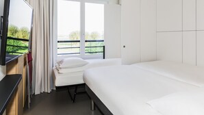 Una camera d'albergo con un letto, una televisione, una finestra con tende e un balcone.