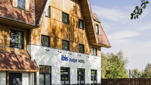 Un hotel moderno con un cartello ben visibile che riporta "ibis budget hotel", caratterizzato da un rivestimento misto in legno e bianco, ampie finestre e un prato curato.