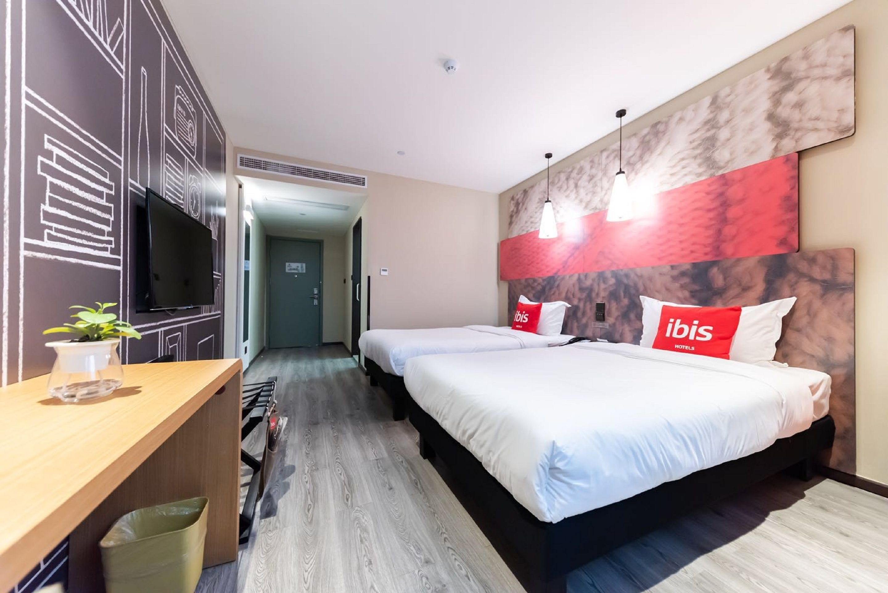 Een hotelkamer met twee bedden, een televisie, een bureau en een plant.