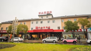 A hotel with a red and white facade, multiple floors, and a parking lot with cars. - ibis Yixing South Renmin Rd (Wuxi)