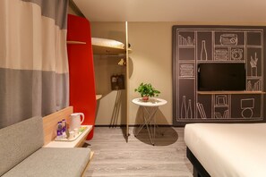Een hotelkamer met een bed, een televisie, een kleintje tafeltje met een plant en een rode scheidingswand.