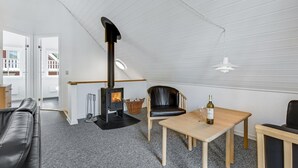A cozy living room with a black leather sofa, a wooden table, a black leather chair, a small wooden table, and a black wood-burning stove. - Marina Fiskenæs Feriepark (Gråsten)