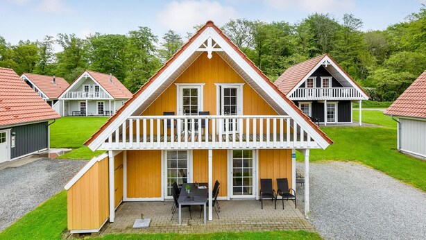 A row of wooden cottages with a central building featuring a balcony and a gravel driveway. - Marina Fiskenæs Feriepark (Gråsten)