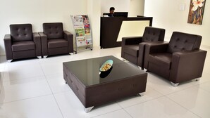 A reception area with a reception desk, two brown leather sofas, a glass coffee table, and a magazine rack. - Sapphire Asta (Hyderabad)