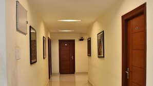 A hallway with a wooden door at the end, framed pictures on the walls, and a light fixture on the ceiling. - Sapphire Asta (Hyderabad)