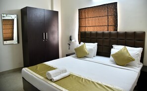 A hotel room with a large wardrobe, a bed with white bedding and two pillows, a bedside table with a phone, and a window with a patterned blind. - Sapphire Asta (Hyderabad)