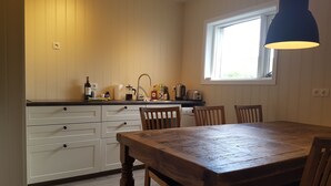 Una cocina con armarios de madera, una mesa de comedor y sillas. Se ve un ventanal con vistas a zonas verdes.