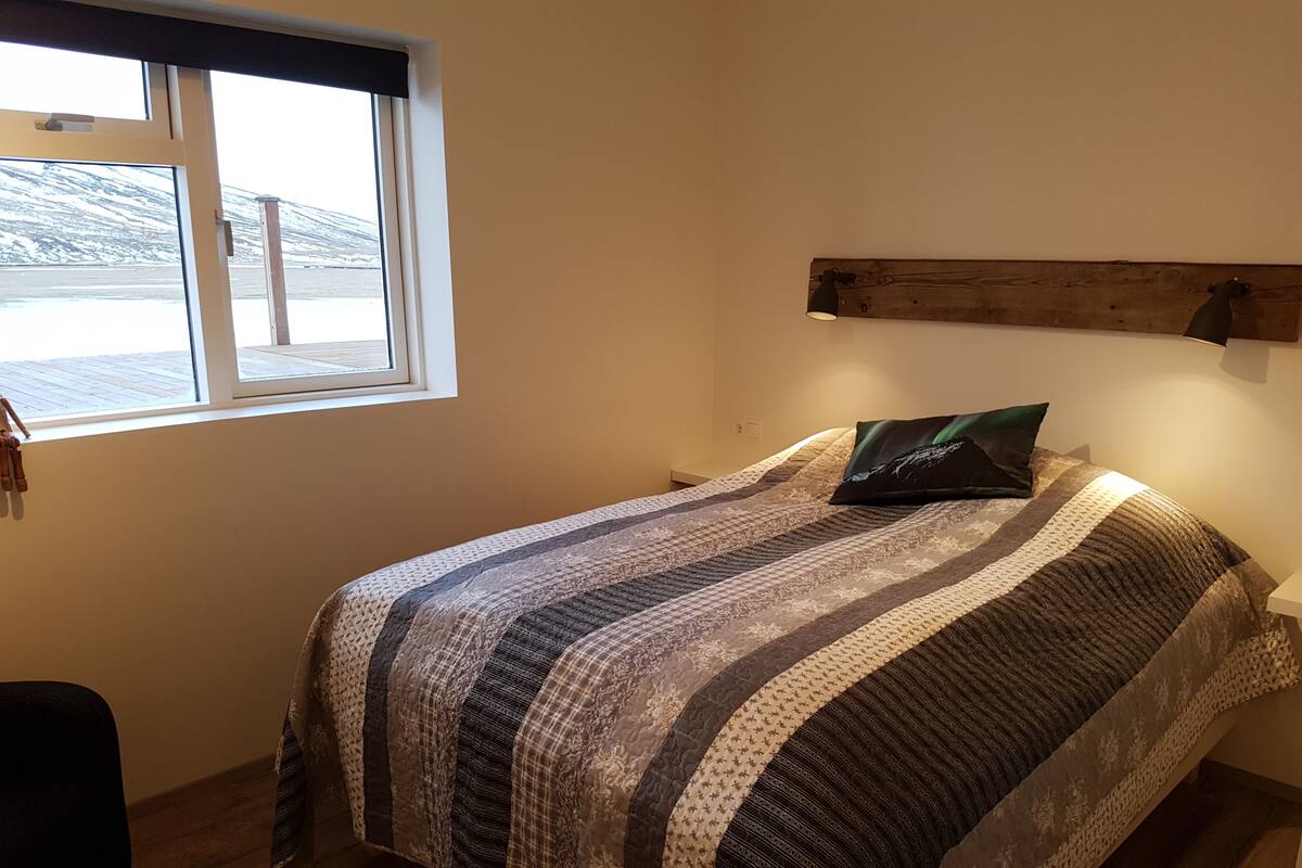 A bedroom with a bed, a window with a view of a snowy landscape, and a wooden headboard.