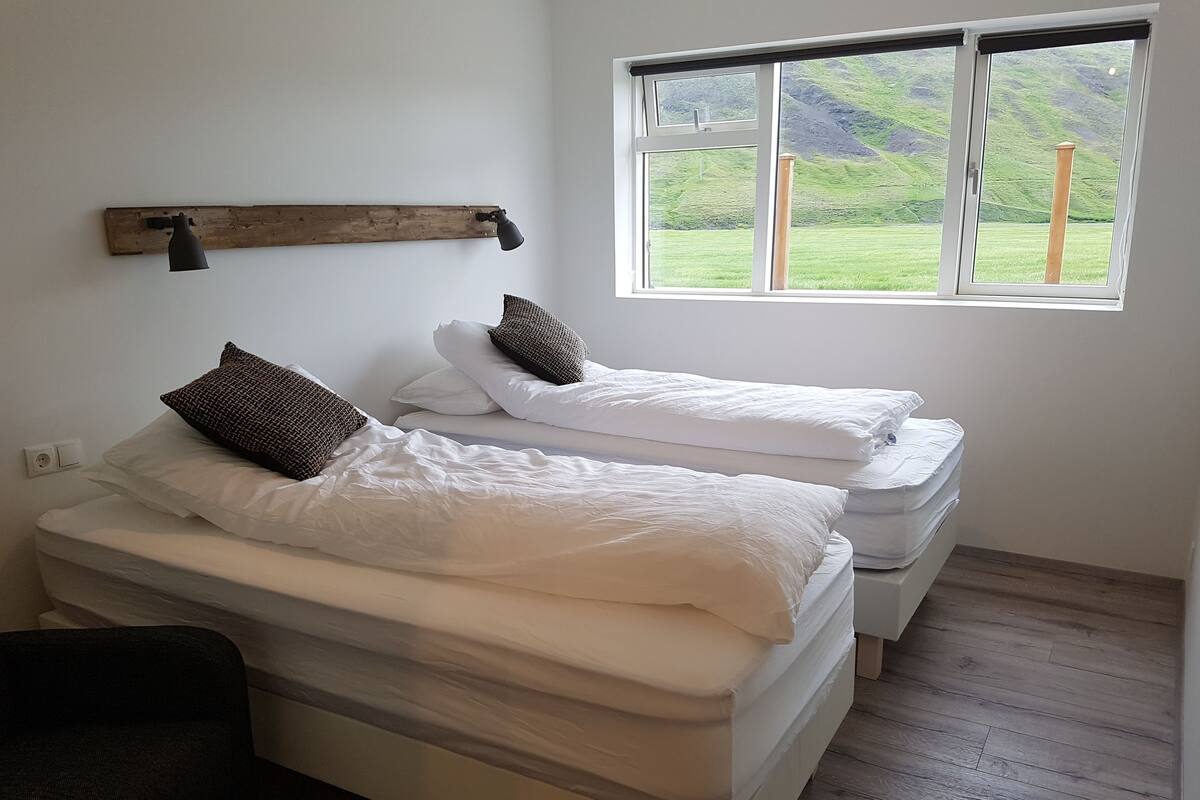 A room with two beds, a wooden bench, and a window with a view of a green landscape.