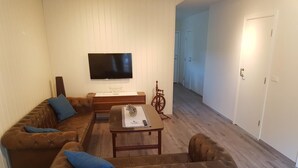 Una sala de estar con un sofá de cuero marrón, una mesa de centro, un televisor de pantalla plana montado en la pared y piso de madera.