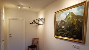 Un pasillo con piso de madera, una silla, una puerta y un cuadro enmarcado en la pared.