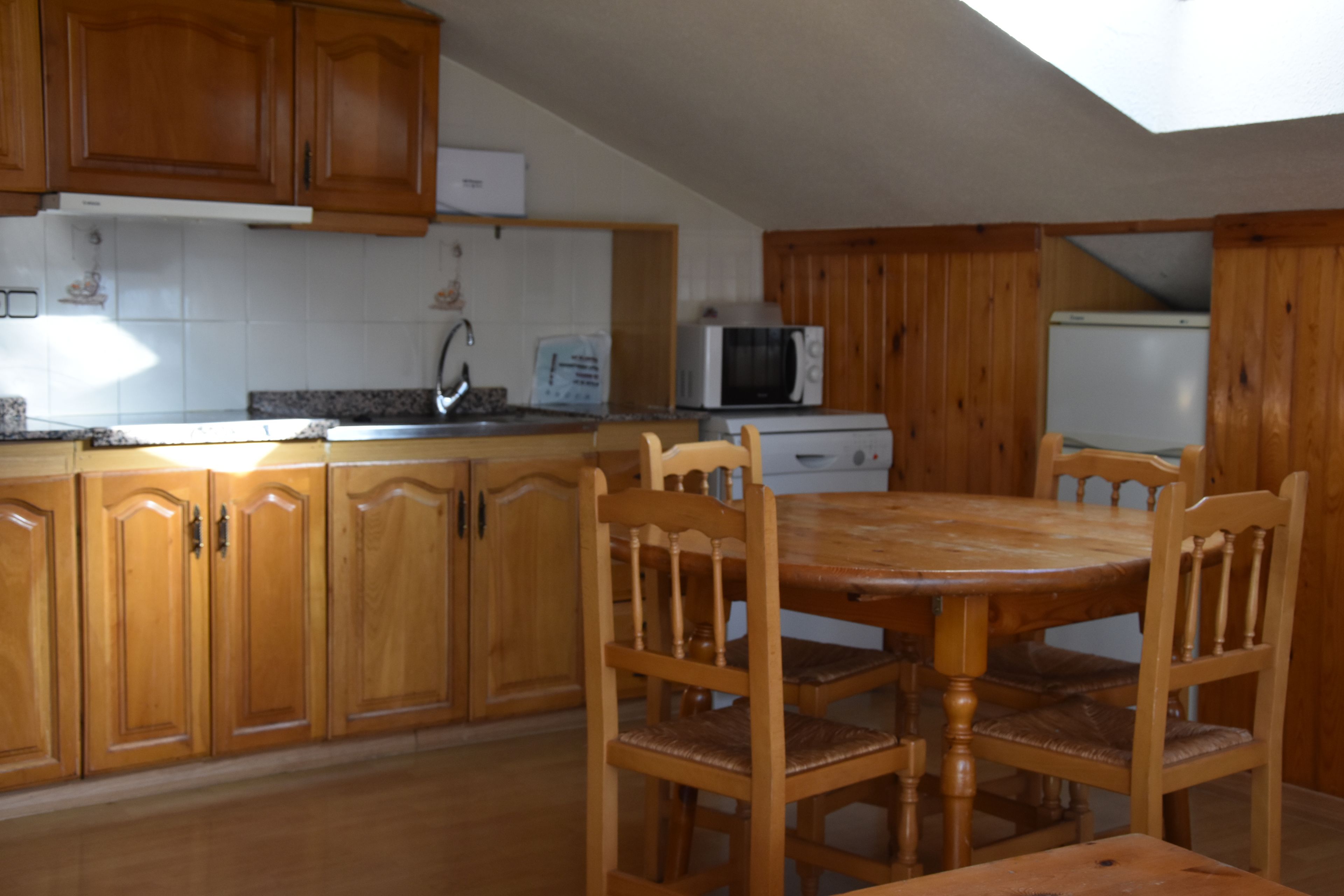 Una cocina con armarios de madera, una mesa de comedor con sillas, un microondas y un refrigerador.