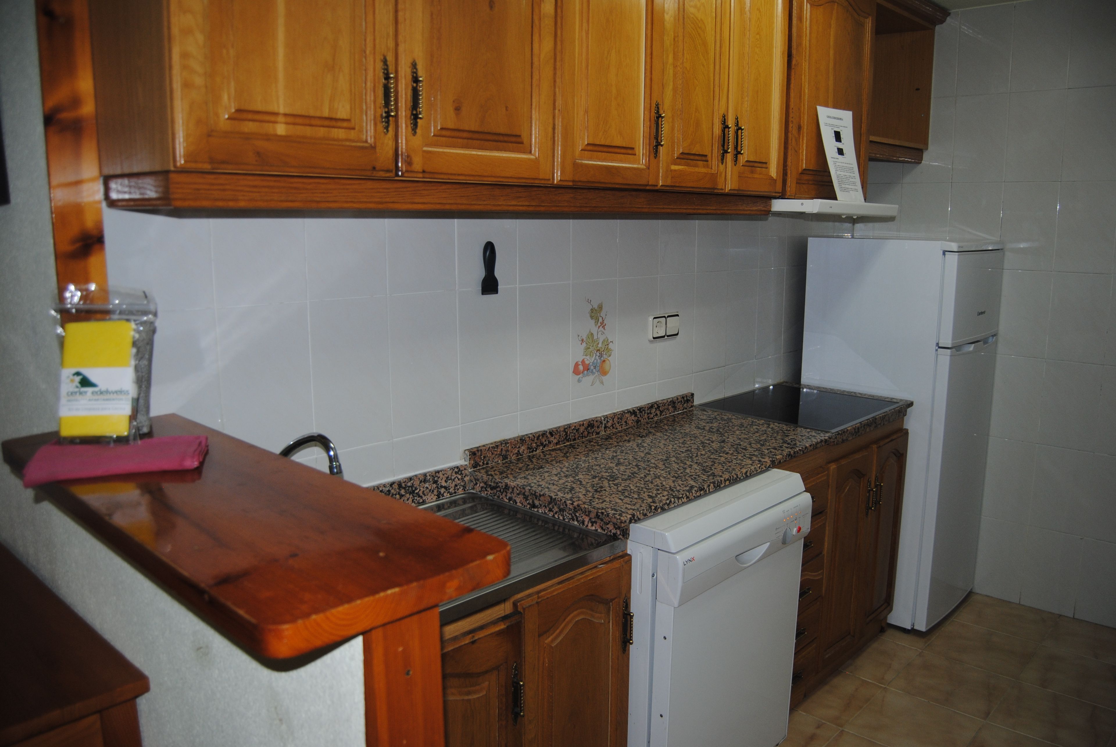 A kitchen with wooden cabinets, a granite countertop, a white dishwasher, and a small sink.