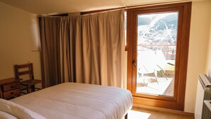 A bedroom with a bed, a wooden chair, a nightstand, and a window with curtains. - Apartamentos SNÖ Edelweiss (Benasque)
