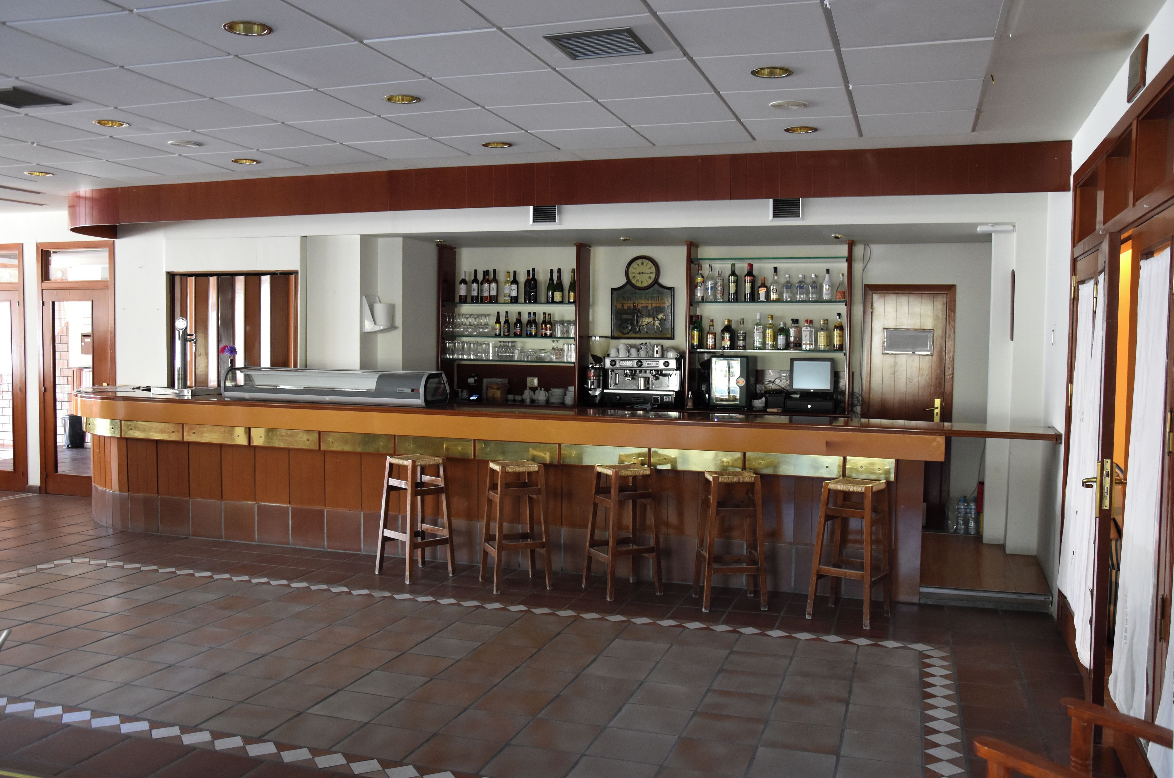 Eine Bar mit einer langen Theke, mehreren Barhocker und einer Auswahl an Flaschen und Gläsern auf Regalen.