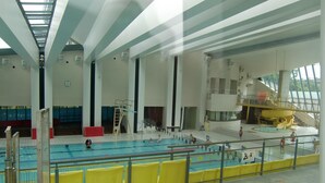 An indoor swimming pool with multiple lanes, a diving platform, and a seating area with yellow barriers. - Guest house KOTONE KYOTO (Kyoto)