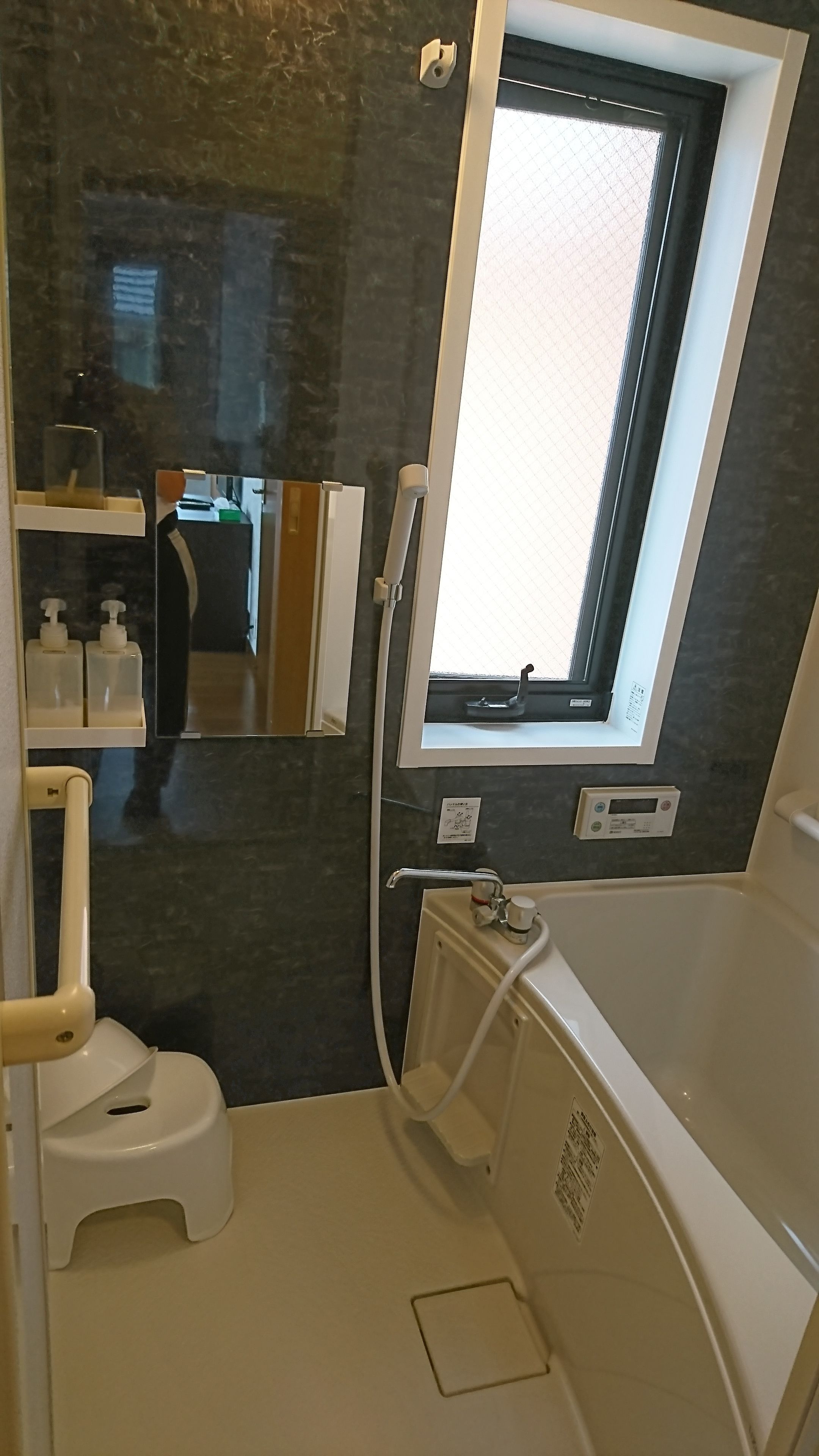 A bathroom with a toilet, a shower, a window, and a mirror.