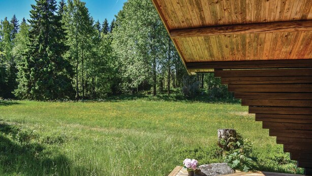 A wooden cabin with a deck, surrounded by a grassy field and dense forest. - Nice home in Månsarp with kitchen (Månsarp)