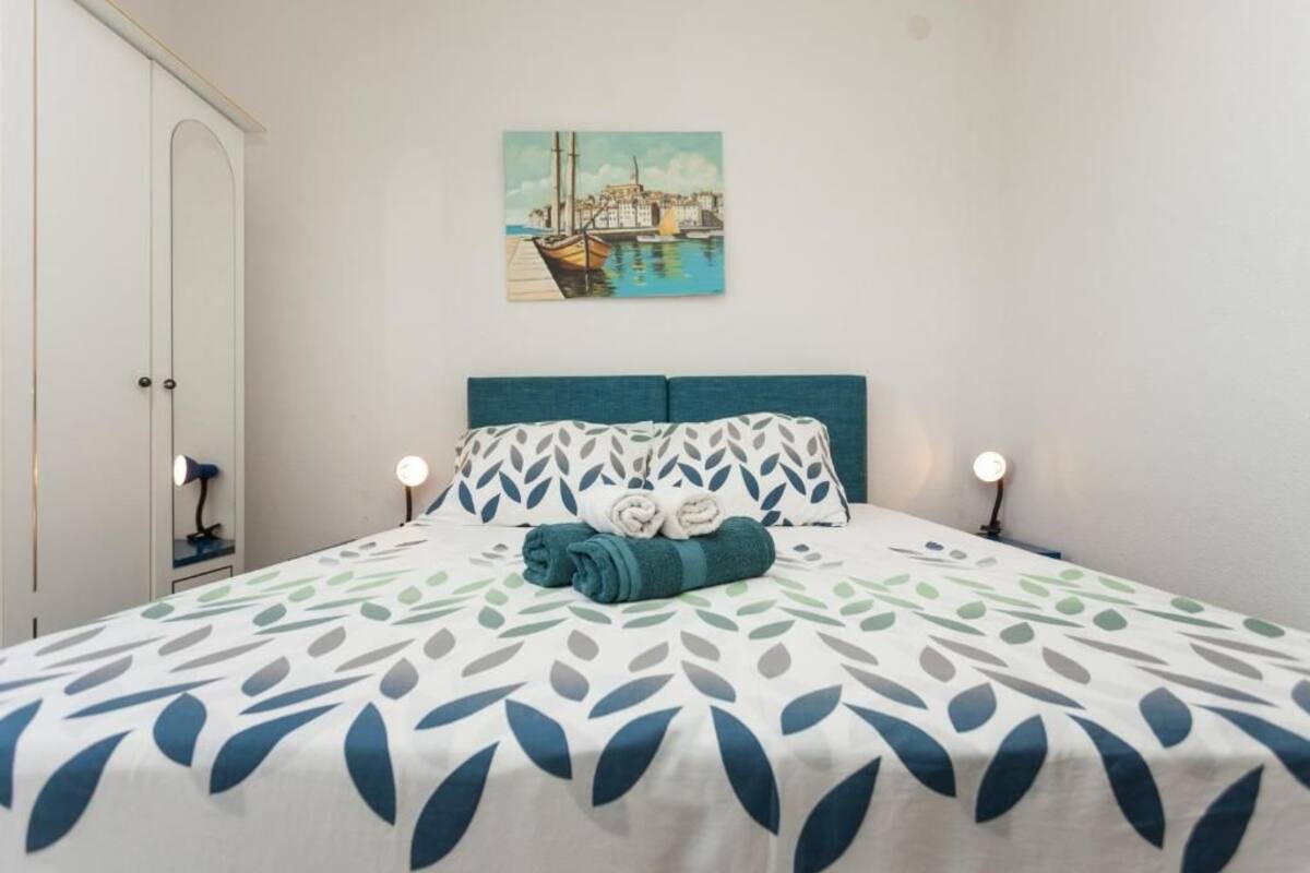 A bedroom with a bed, a painting of a harbor, and a wardrobe.